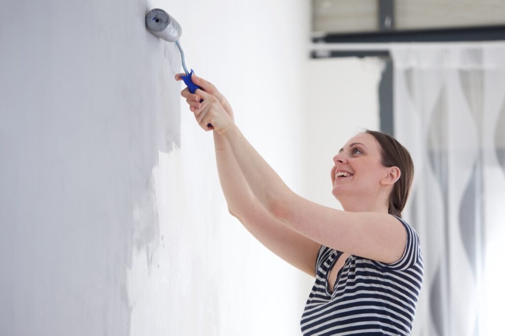 happy young woman painting wall in room